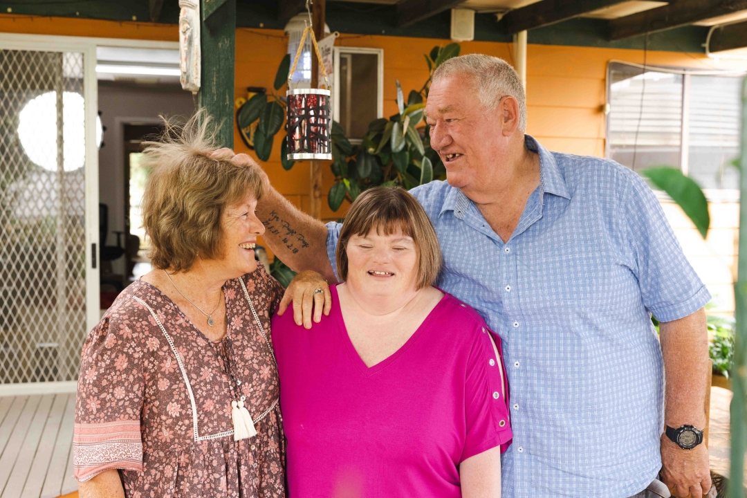 An older couple standing either side of woman with Down syndrome