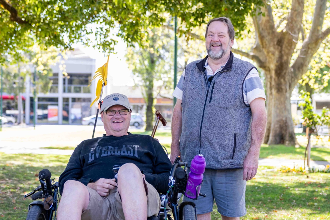 Michael is seated in a recumbent bike, and his support worker Kevin is standing next to him on the right